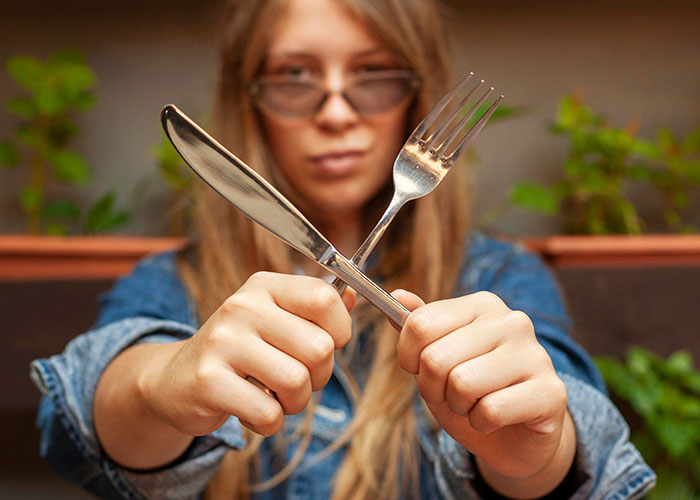 Woman holding knife and fork crossed, symbolizing American dining habits abroad.