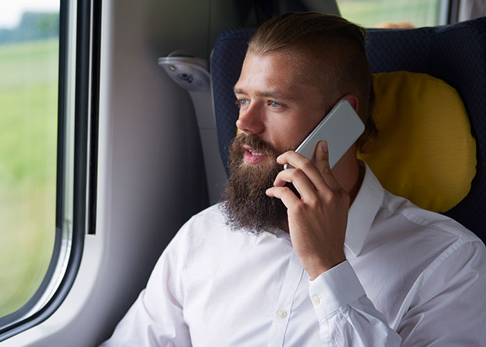 Man on a train, wearing a white shirt, talking on the phone, showcasing behaviors Europeans say reveal Americans abroad.