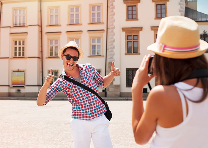 Tourist in sunglasses and hat posing for photo in European square, showcasing American travel style.