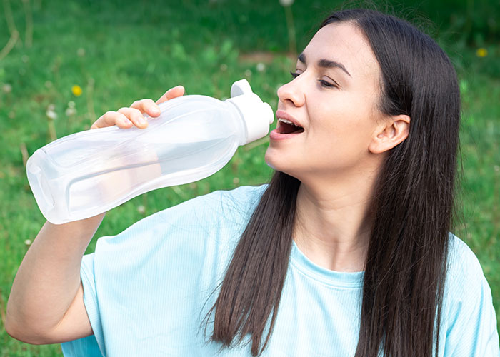 Woman drinking from a large water bottle outdoors, highlighting American travel habits.