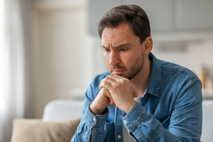 Pensive man in a denim shirt reflecting on family decisions.