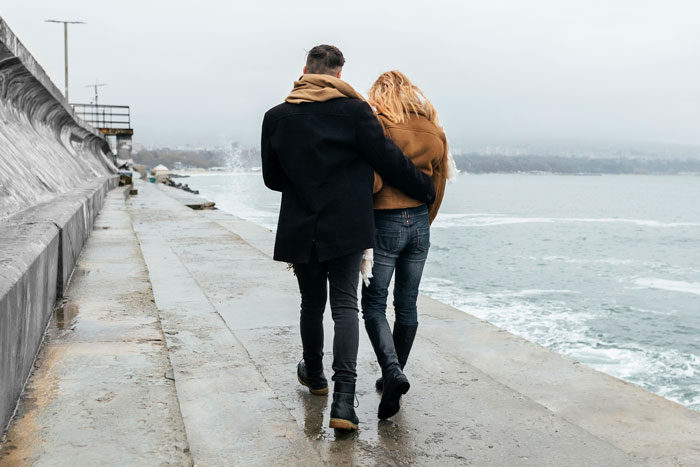 Couple walking by the sea on a cloudy day, highlighting relationship and breakup before Valentine's.