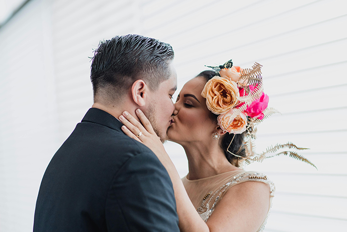 Bride with floral hairpiece kissing groom, representing excluded wedding step causing upset with step mother-in-law.