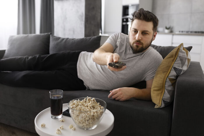 Man relaxing on a couch with a remote, snacks, and a drink, illustrating explain-adult-moments.