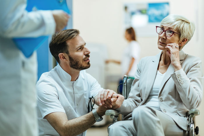 Man comforting elderly woman in a wheelchair, holding hands, conveying loyalty and support in a hospital setting.