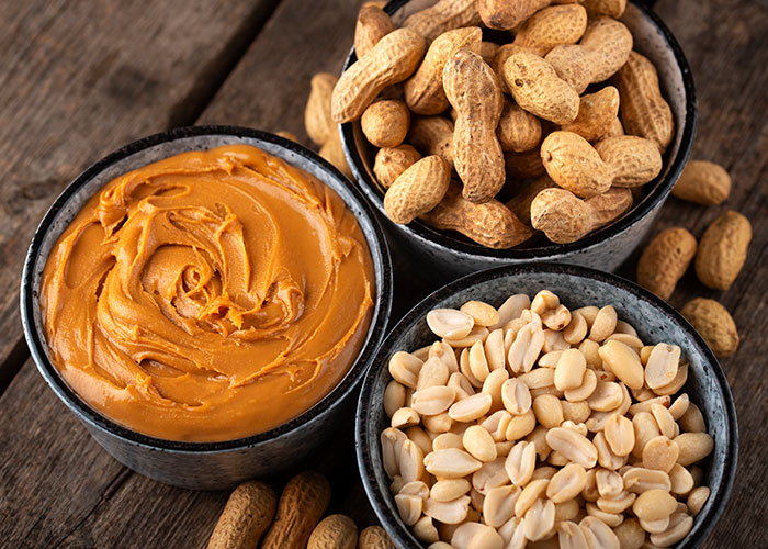 Peanuts and peanut butter displayed in bowls on a wooden surface.