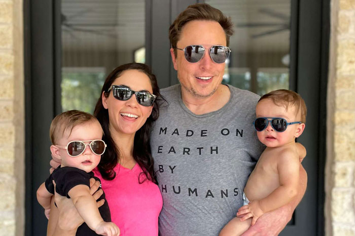 I don't know who the individuals in the image are. A man and a woman, both in sunglasses, smiling and holding two babies outside. I don't know who the individuals in the image are. A man and a woman, both in sunglasses, smiling and holding two babies outside.