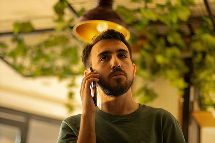 Man with beard talking on phone indoors, appearing serious, relating to hubby confronting family about pregnant wife treatment.