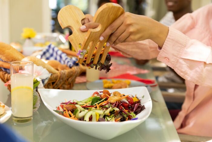 Child serving salad with oversized wooden forks, adding a touch of comedy to the lunch table setting.