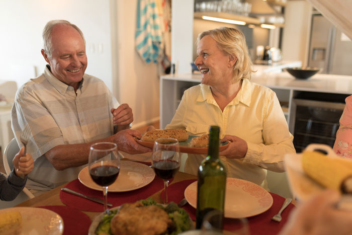 Older couple sharing bread at family anniversary celebration, surrounded by wine and food.