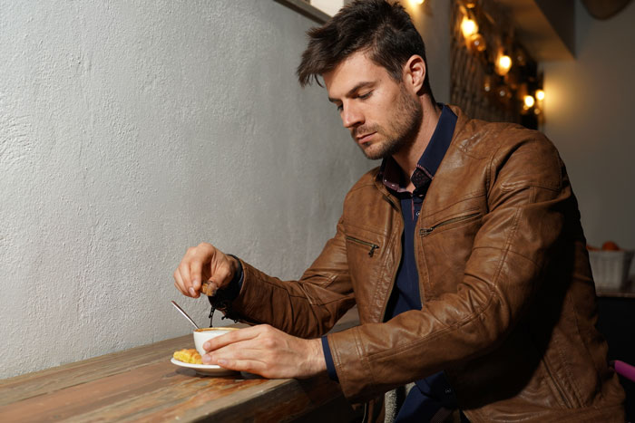 Man in a leather jacket alone at a caf&eacute; table, symbolizing personal choices affecting relationships.