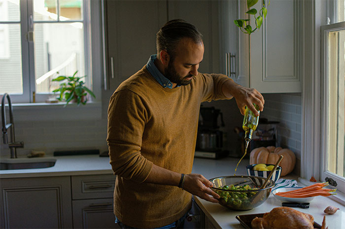 Man in kitchen pouring olive oil on salad, reflecting on the woman furious about physical consequences of accident caused by fiancé. Man in kitchen pouring olive oil on salad, reflecting on the woman furious about physical consequences of accident caused by fiancé.