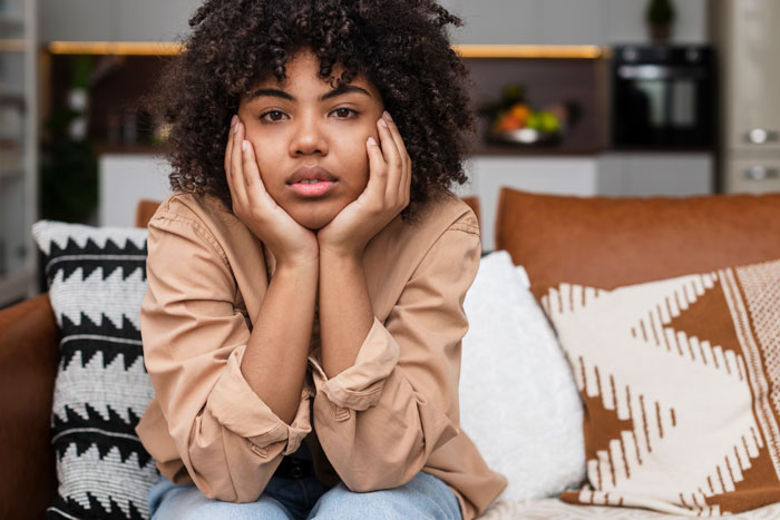 Woman sitting on a sofa, looking contemplative, with focus on relationship dynamics.