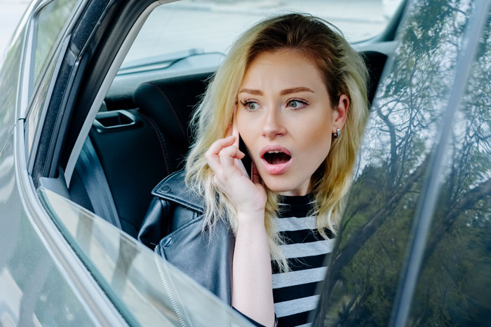 Young woman in car, looking shocked, on phone discussing weird behavior with motives.