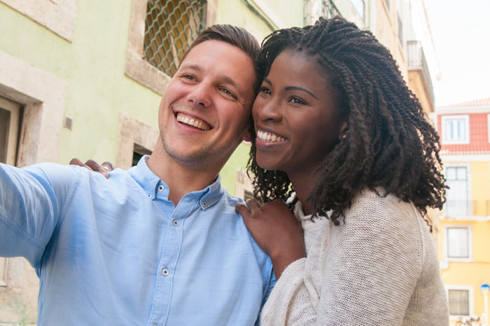 Man and woman smiling outdoors, capturing a selfie together.