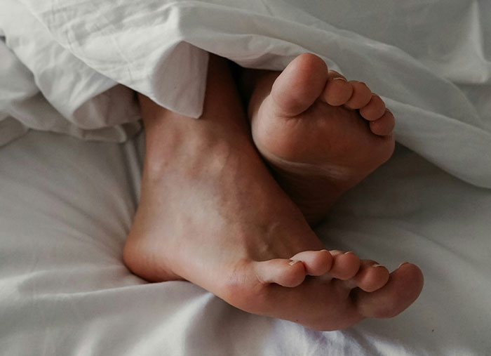 Feet peeking out from under white sheets, symbolizing comfort and rest amid reflections on ending friendships.