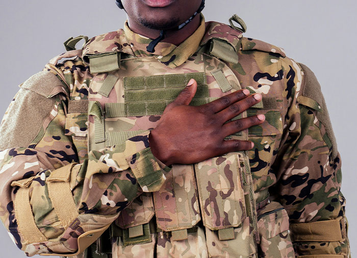 Person in camouflage uniform with hand on chest, a gesture symbolizing respect and camaraderie in friendships.