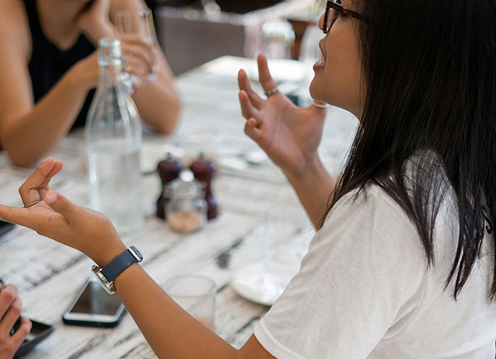 Woman gesturing during a discussion at a table, illustrating friendships.