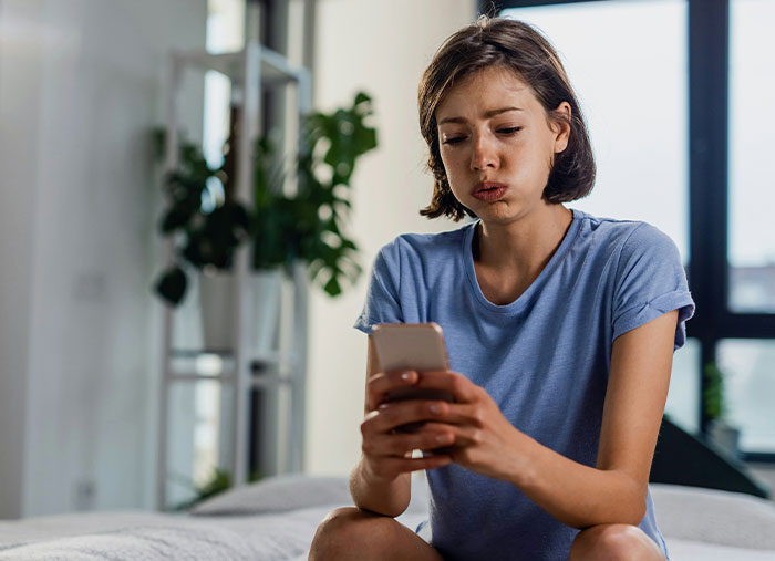 A woman in a blue shirt looks thoughtful while reading a message on her phone, reflecting on friendships.