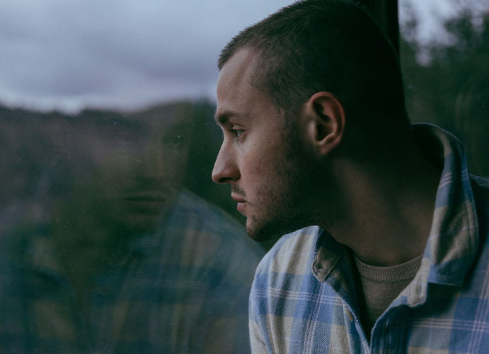 Man in plaid shirt gazing out a window, reflecting on ending friendships.