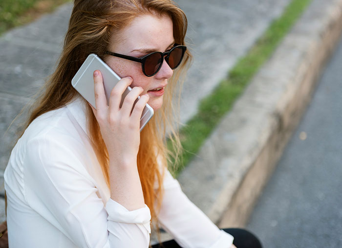 Person sitting on a curb, wearing sunglasses, talking on a phone; illustrating the end of great friendships.
