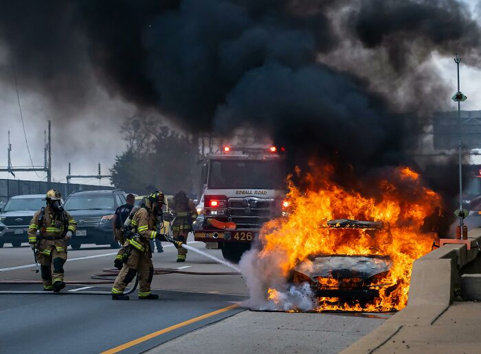 Firefighters responding to a car fire on a highway, with flames and smoke, highlighting potential mistakes by first responders.