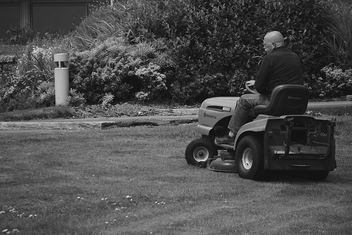 Man driving a lawnmower on grass in a garden setting, highlighting potential first responder safety oversights.