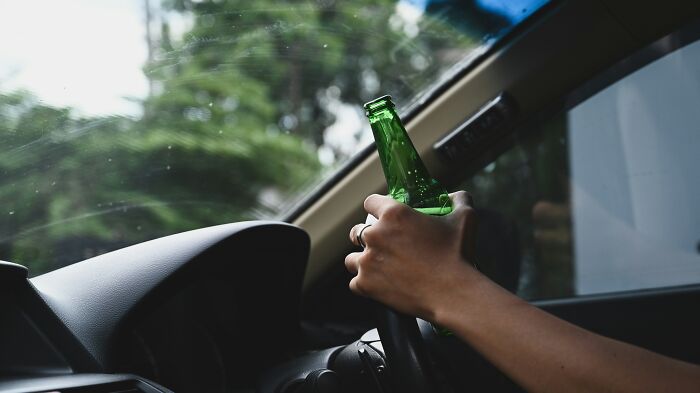 Person holding a beer bottle inside a car, highlighting dangerous mistakes EMTs and first responders encounter.
