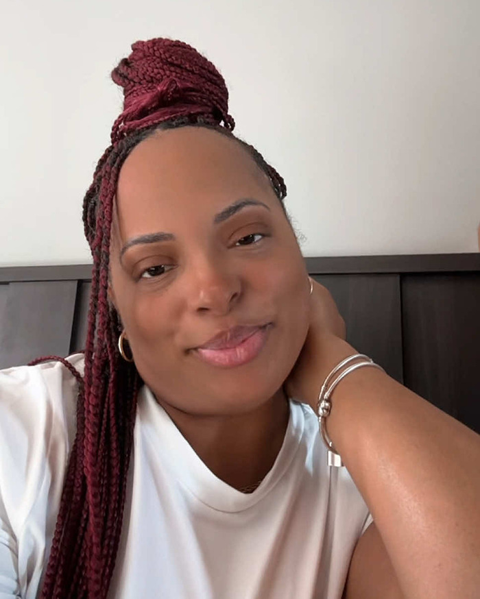 Smiling woman with braided hair and white shirt, sitting indoors.