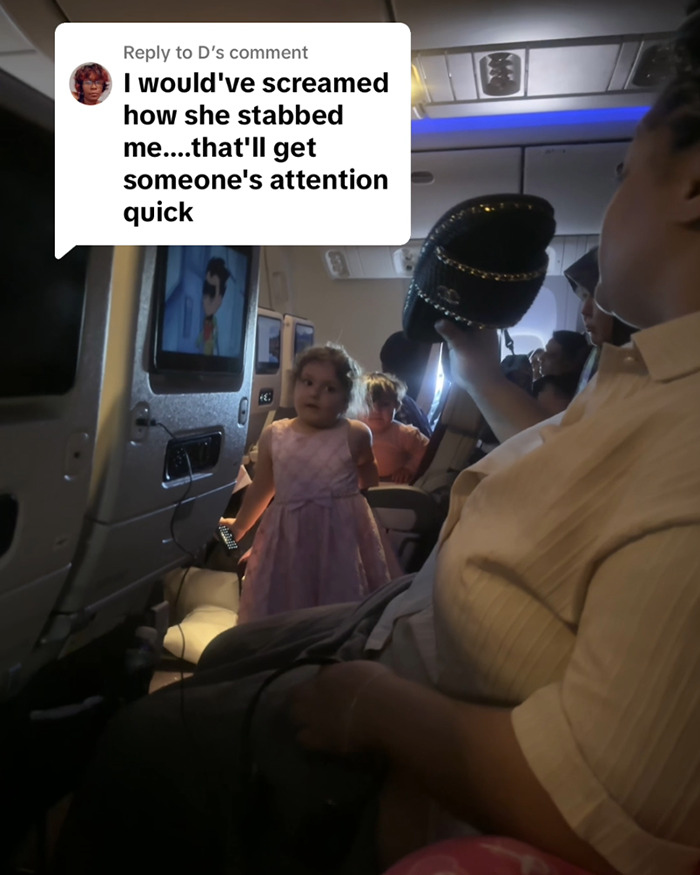 Child in a pink dress stands in airplane aisle, onboard scene with passengers seated and overhead comment about a stabbing incident.