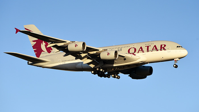 Qatar Airways plane flying against a clear blue sky, representing passenger experience.