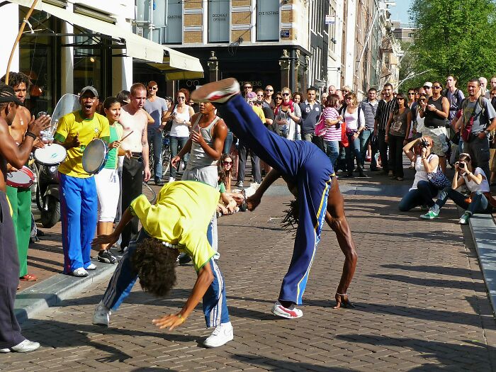 Street performers in vibrant outfits showcasing acrobatics, attracting a large crowd on a sunny day.