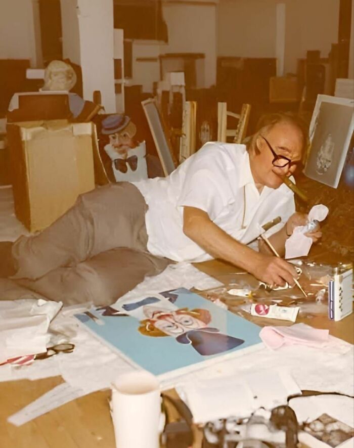 Man painting while smoking a cigar, surrounded by art materials and finished pieces; concept of forbidden stories.