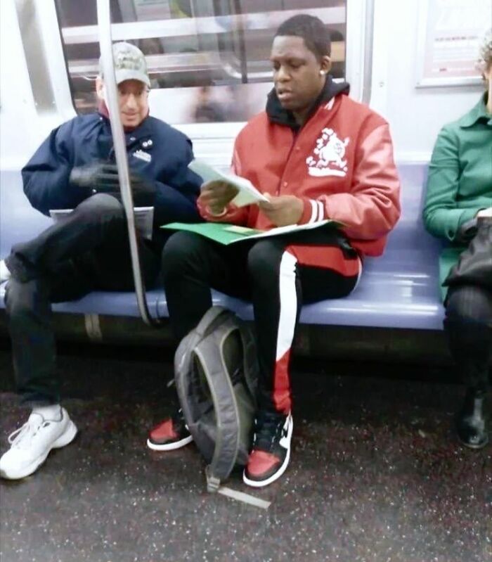 Man in a red jacket reading "Forbidden Stories" while sitting in a subway.
