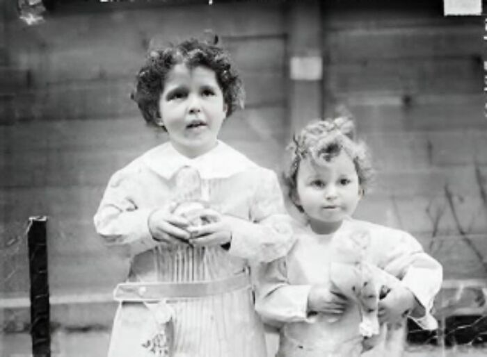 Two children in vintage attire holding toys, portraying a scene from interesting forbidden stories.