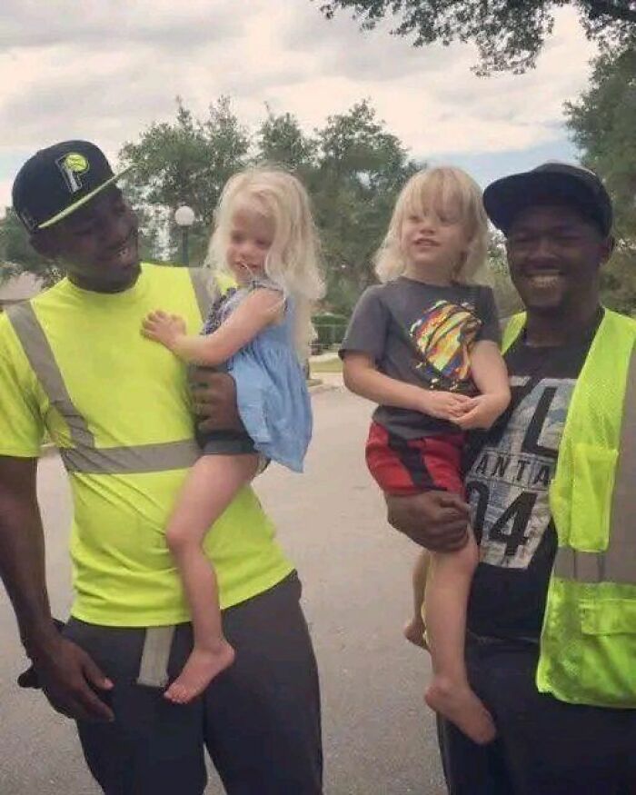 Two smiling men in reflective vests holding children, evoking stories of friendship and community.