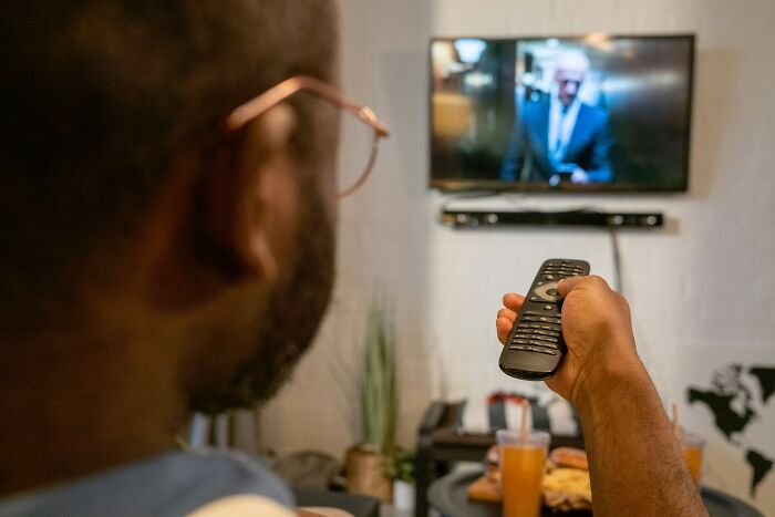 Man with remote watching TV, possibly experiencing USA culture shock.