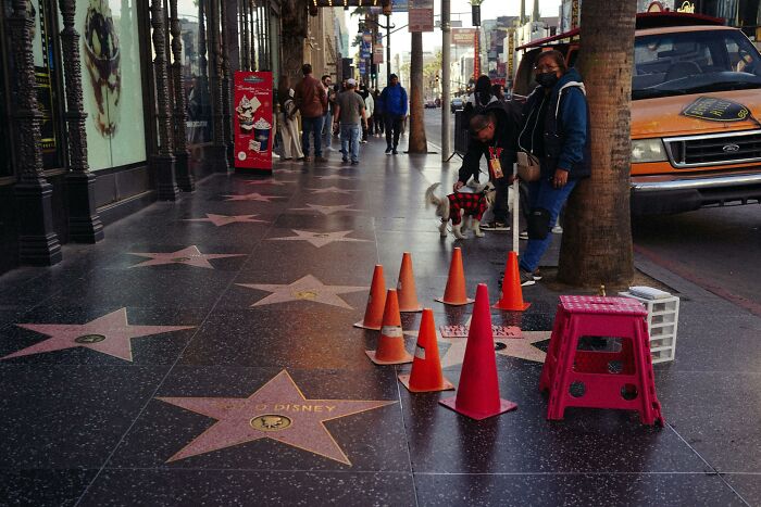 Sidewalk in USA with stars, traffic cones, and people. Cultural details highlight tourism and pedestrian activity.