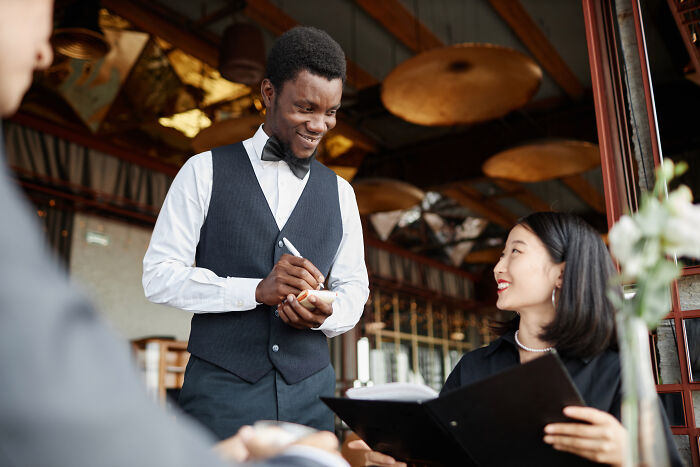 Waiter taking an order from a smiling customer in a restaurant, highlighting culture shocks in USA dining experiences.