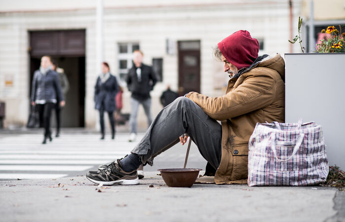 Homeless person sitting on street, experience of culture shock in USA.