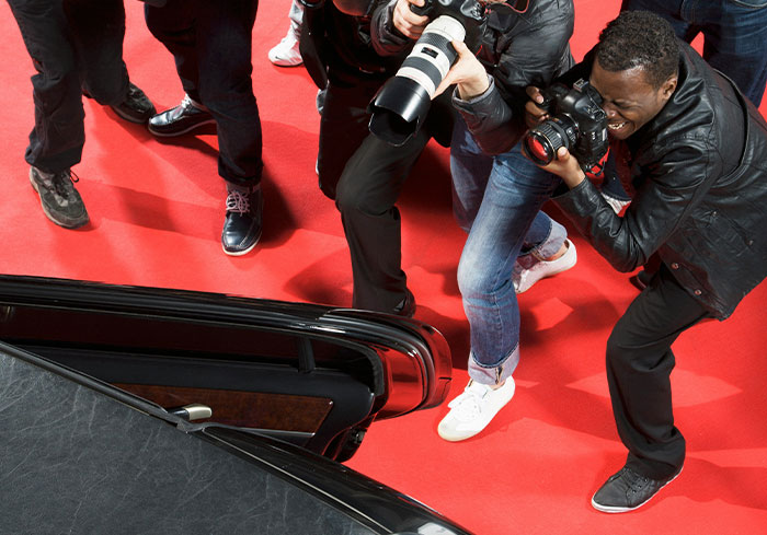 Photographers crowding a car on the red carpet, capturing the moment for a celebrity confession story.
