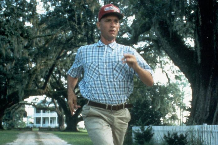 A man in a plaid shirt and red cap runs down a tree-lined path in an emotionally impactful movie scene.