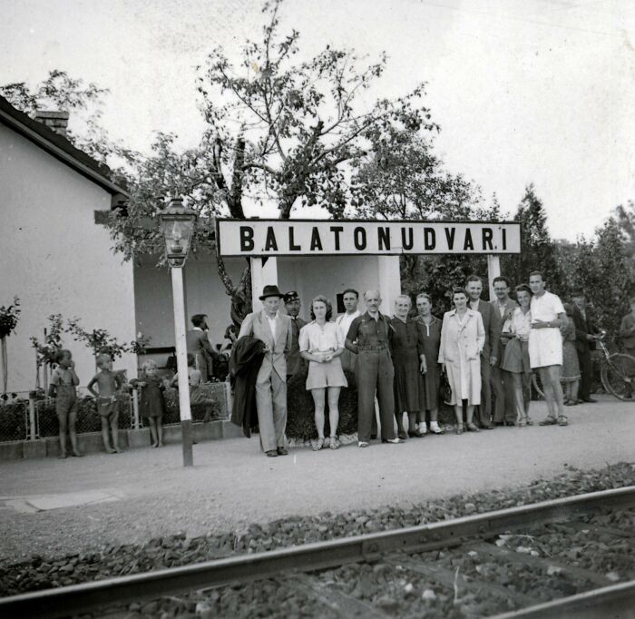 Group of people standing at a Balatonudvari train station in Europe, showcasing life in Europe 100 years ago in a black and white photo.