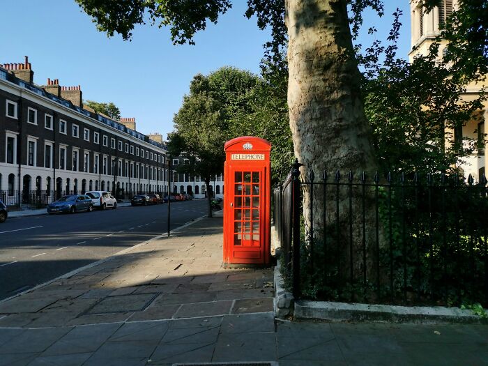 Red phone booth on a quiet street, symbolizing making a call as a common activity 30 years ago.