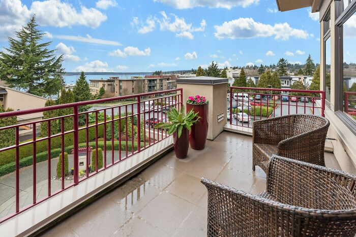 Balcony view with wicker chairs, overlooking a scenic neighborhood on a sunny day.