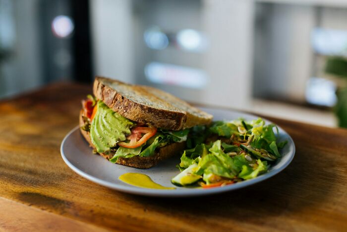 Avocado sandwich with salad on a plate, placed on a wooden table.