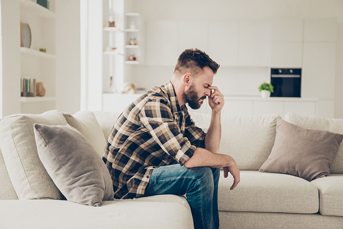 Man sitting on a sofa looking stressed about babysitting situation.