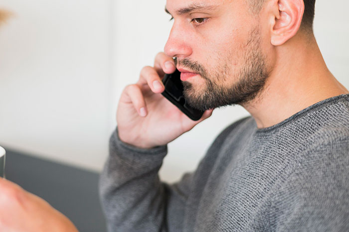 Man talking on phone, concerned expression, holding a mug, addressing babysitting and disappearance issue.