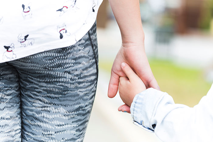 Woman holding child's hand, wearing patterned leggings, signifying babysitting trust.