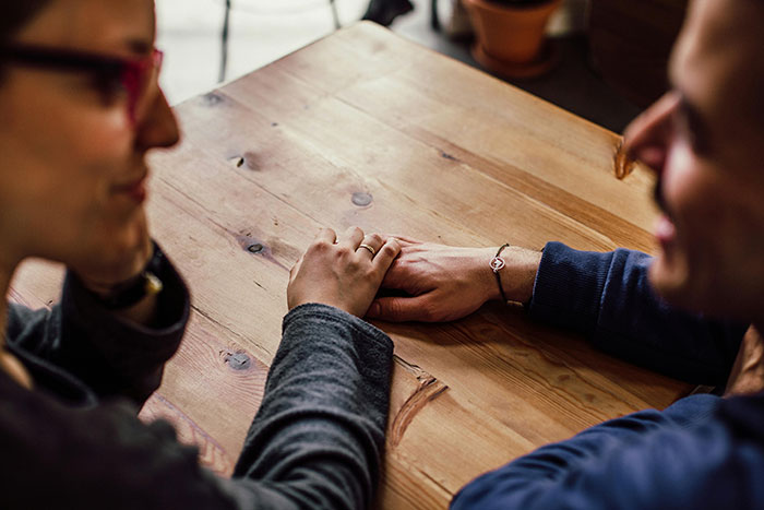 Two friends discussing birthday plans at a wooden table, one wearing a bracelet, focusing on a diet conversation.